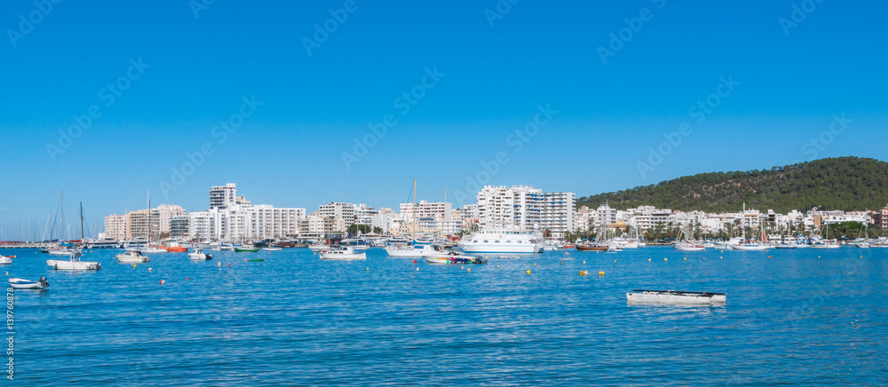 Boats, small yachts & water craft of all size in marina of Sant Antoni De Portmay.   Morning of warm sunny day in the harbour.  Bright town of  Sant Antoni de Portmany, Balearic Islands, Spain.