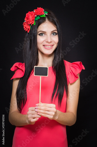Beautiful woman with a wreath of red flowers holds a wooden plaque. Close-up