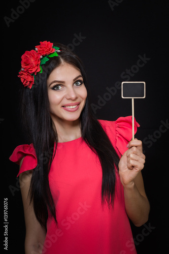 Beautiful woman with a wreath of red flowers holds a wooden plaque. Close-up