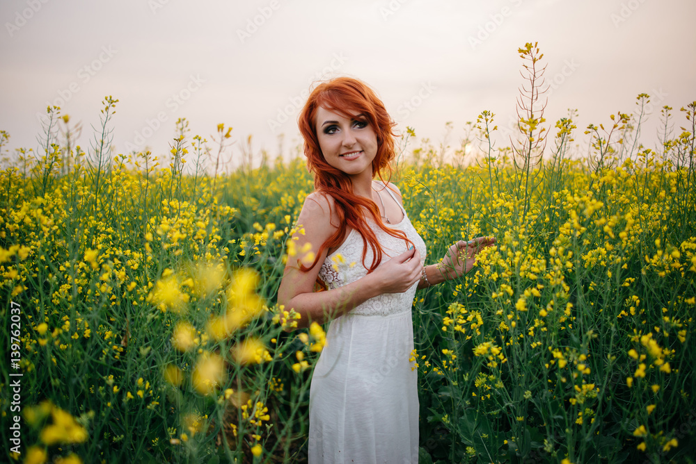 Fototapeta premium Young red-haired woman in a rapeseed field