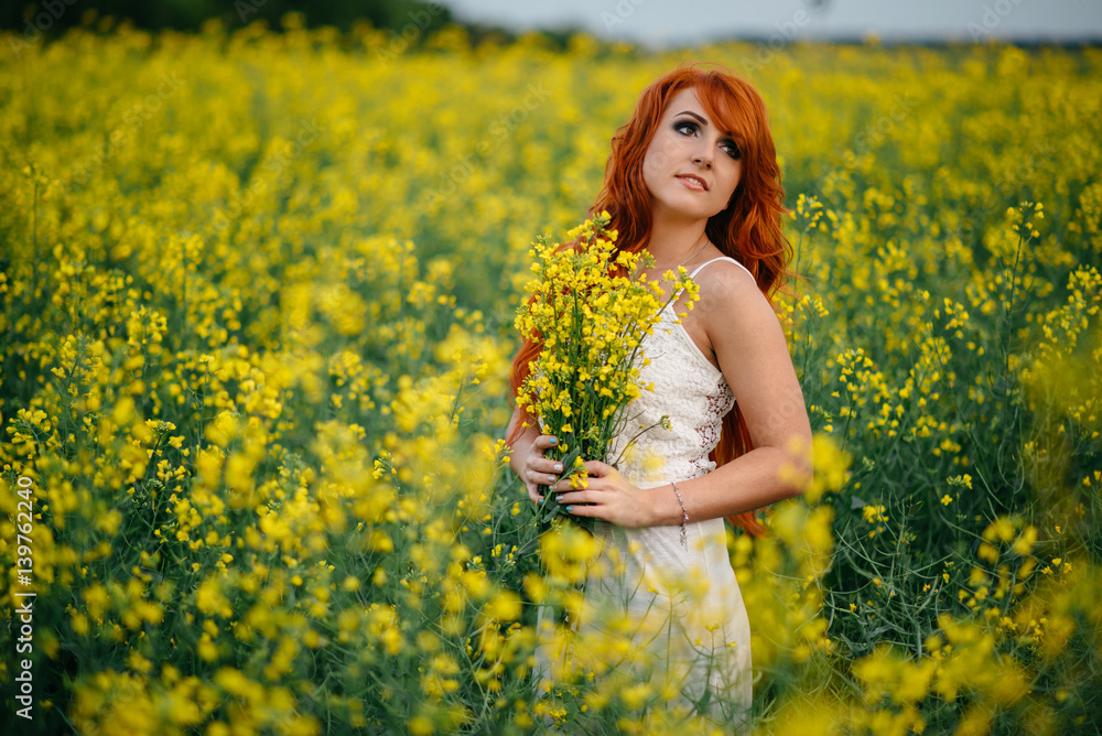 Fototapeta premium Young red-haired woman in a rapeseed field