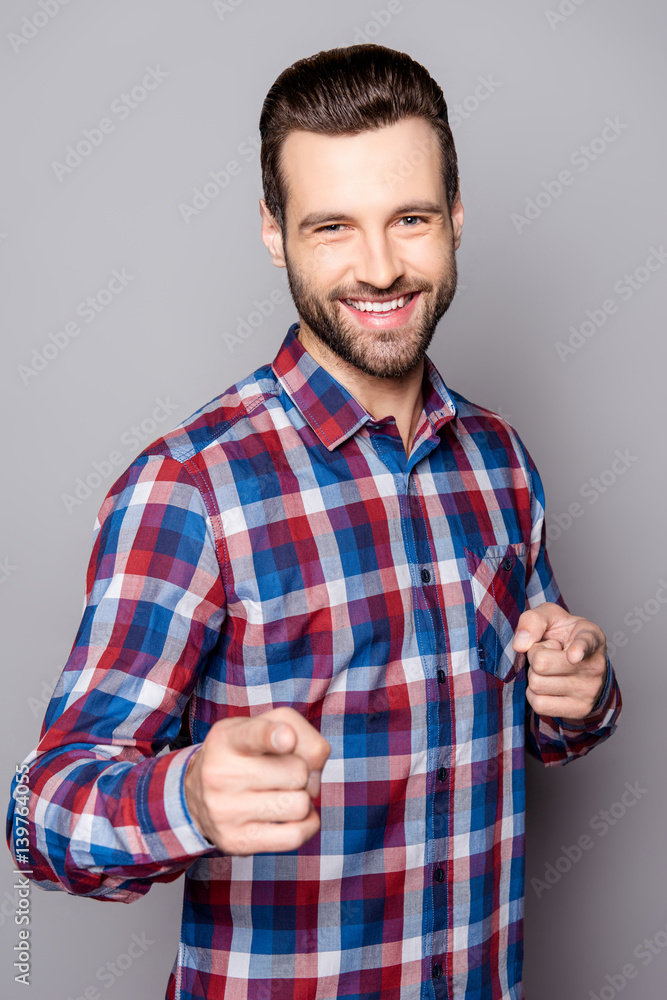 A close up portrait of young smiling man standing against gray background and pointing at you with his fingers A close up portrait of young smiling man standing against gray background and pointing at you with his fingers