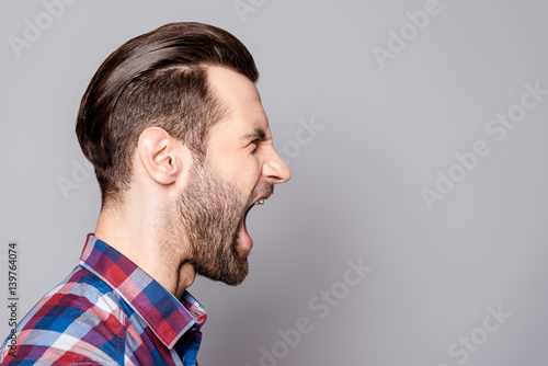 Billede på lærred A half-face portrait of a young bearded yelling man with fashionable haircut iso