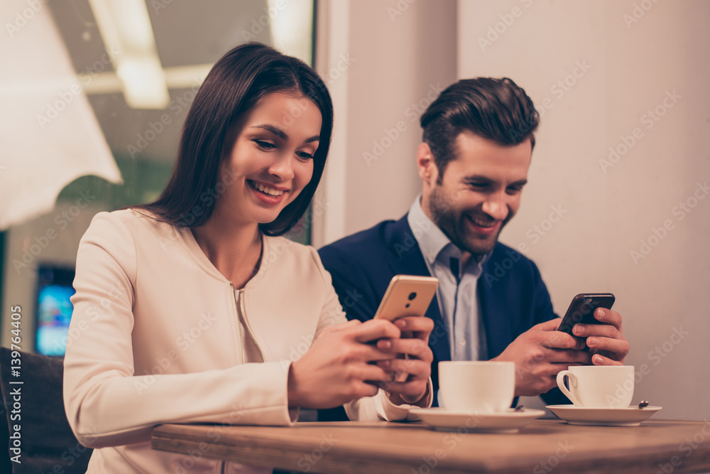 Cheerful couple sitting in a cafe holding phones Cheerful couple sitting in a cafe holding phones