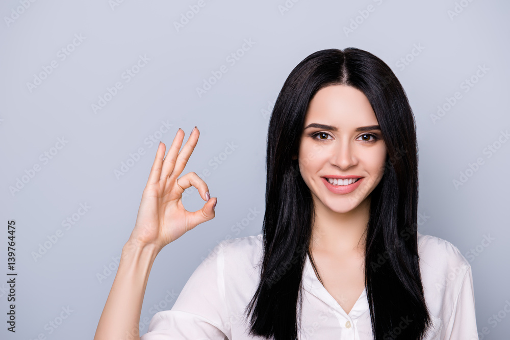 Portrait of beautiful cute young woman with toothy smile and black hair showing ok sign with fingers Portrait of beautiful cute young woman with toothy smile and black hair showing ok sign with fingers