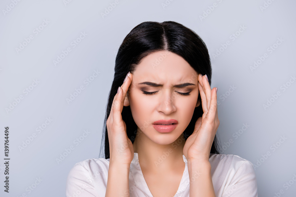 Portrait of tired beautiful young woman with black hair suffering from headache on gray background Portrait of tired beautiful young woman with black hair suffering from headache on gray background