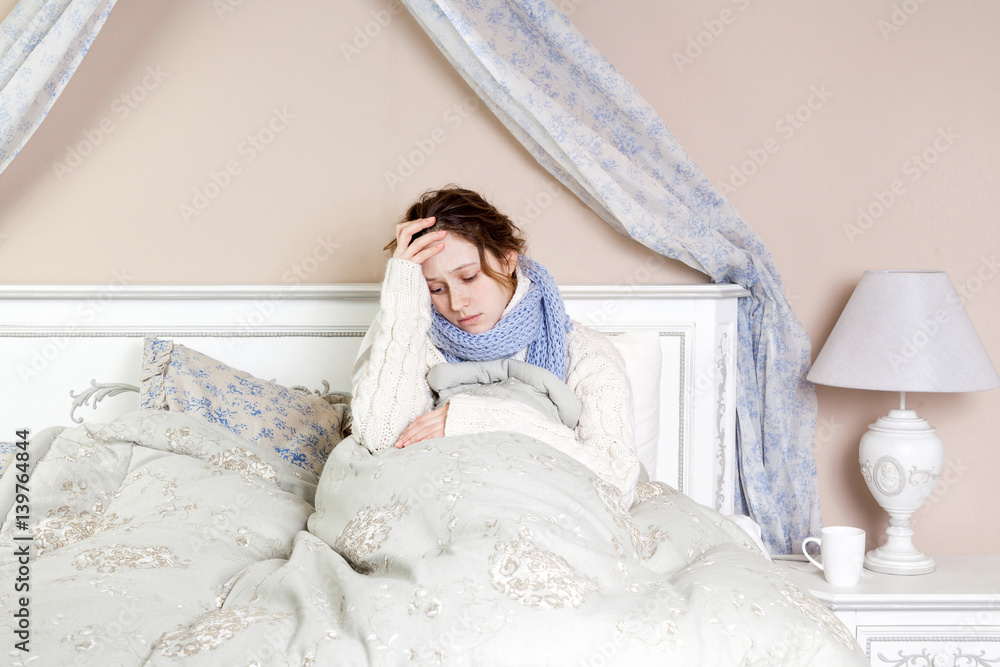 Flu or cold. Closeup top view image of frustrated young woman with blue scarf and suffering from terrible headache while lying in bed. Flu or cold. Closeup top view image of frustrated young woman with blue scarf and suffering from terrible headache while lying in bed.