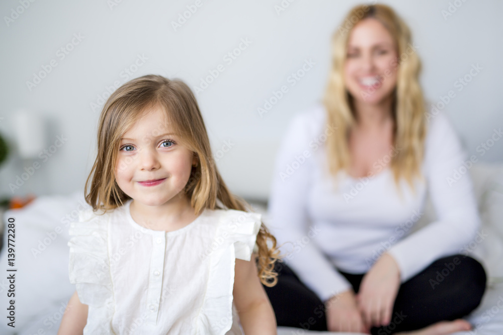 Cute little girl and her mother lying on a bed