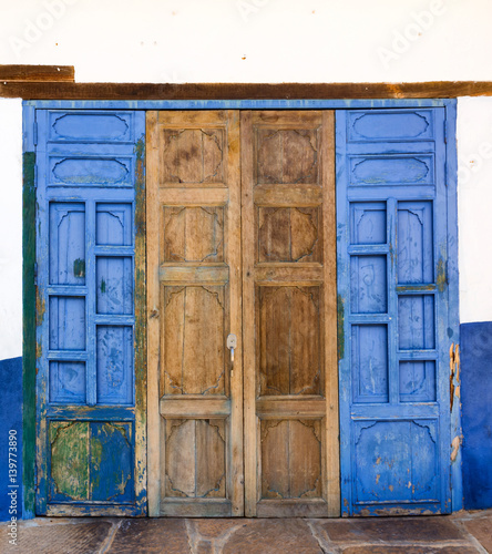 A mosaic of blue and worn wooden textures on intricately latticed doors in Barichara, Colombia.