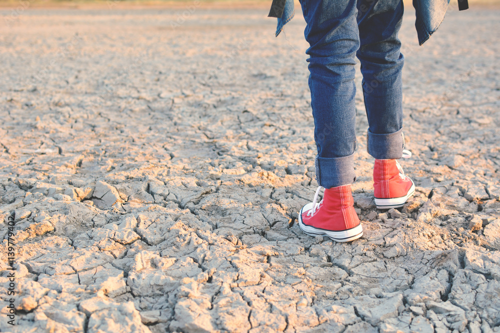 Fototapeta premium Feet sneaker on crack dry ground, concept drought