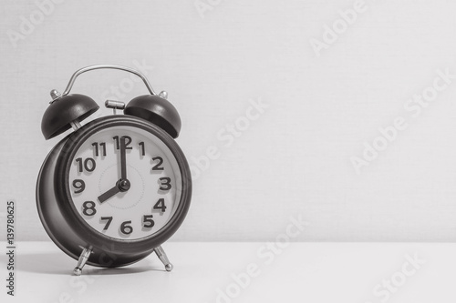 Closeup alarm clock for decorate in 8 o'clock on white wood desk and cream wallpaper textured background in black and white tone with copy space