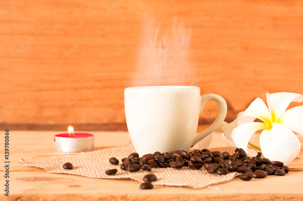 the hot coffee in the white cup on wooden table with coffee seed and red candle the hot coffee in the white cup on wooden table with coffee seed and red candle