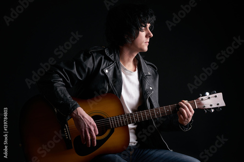 Rockstar in biker leather jacket playing solo on acoustic guitar.