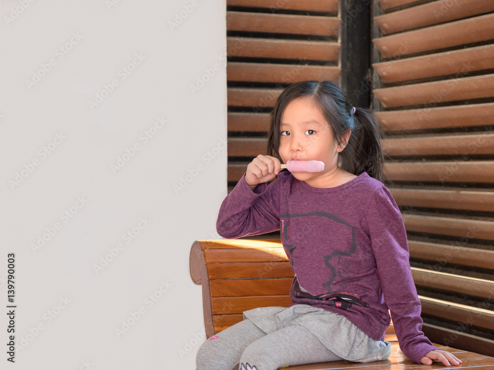 Little Asian girl eating ice cream, wood shade stripes background Little Asian girl eating ice cream, wood shade stripes background