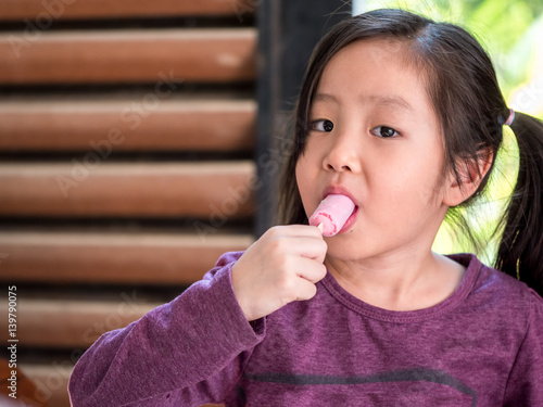 Little Asian girl eating ice cream, wood shade stripes background