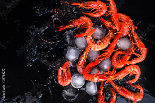 Fresh raw shrimps on black background with ice - Food background with copyspace.