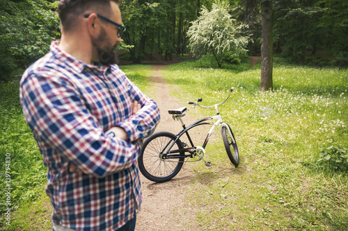 Hipster man standing at park looking at bicycle photo