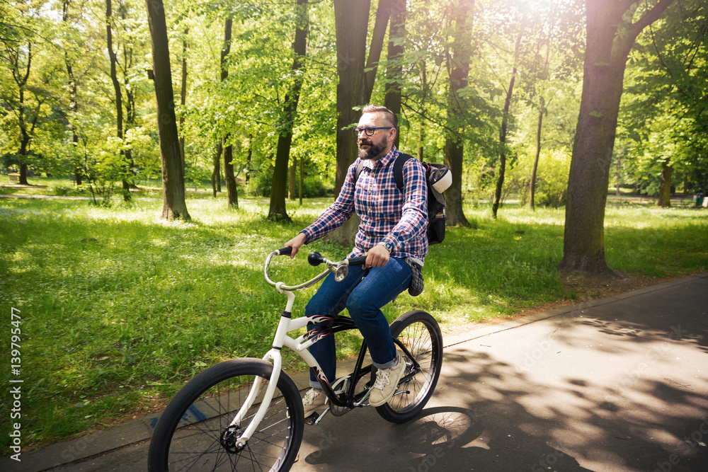 Fototapeta premium Trendy hipster man riding bicycle through park