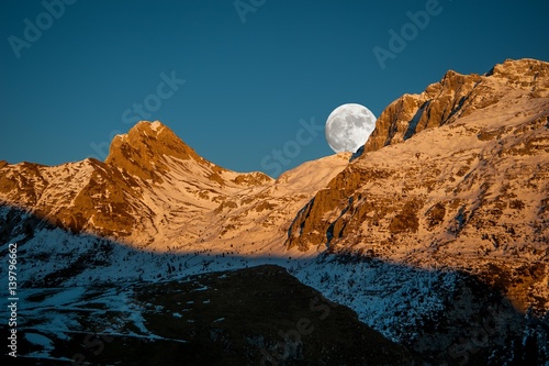 snowy mountain at sunset with full moon