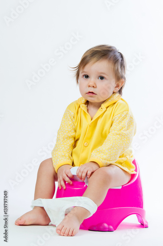 Little smiling girl sitting on a pot. Isolated on white background.