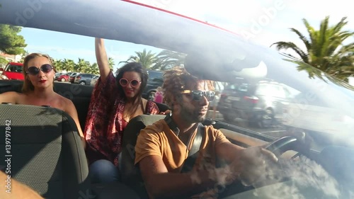 Young people singing and dancing in red convertible looking for parking space 