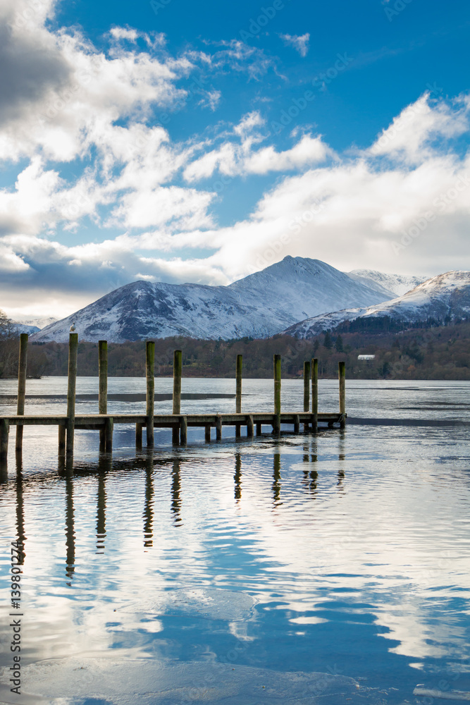 Naklejka premium A pier reflected in Lake Derwent with snow covered mountains in the English Lake District