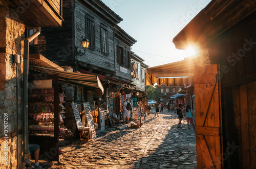 People walk through pedestrian cobblestone streets of ancient Nessebar with cafe, restaurant and souvenir shops at sunset. photo
