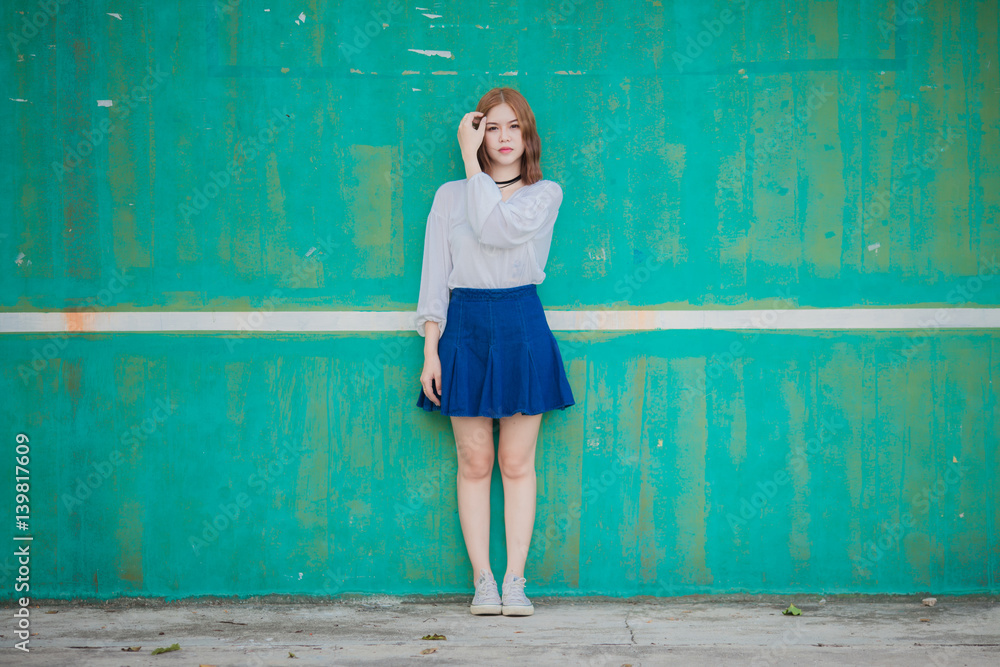Fototapeta premium Portrait of young hipster Asian girl posing in the Dirty blue wall background