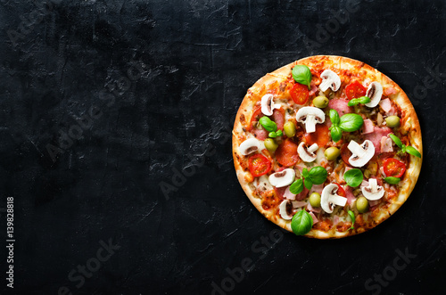 Fresh italian pizza with mushrooms, ham, tomatoes, cheese, olive, basil on black concrete background, rustic table. Copy space. Homemade with love. Fast delivery. Recipe and menu. Top view