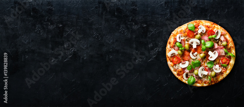 Fresh italian pizza with mushrooms, ham, tomatoes, cheese, olive, basil on black concrete background. Copy space. Homemade with love. Fast delivery. Recipe and menu. Banner.