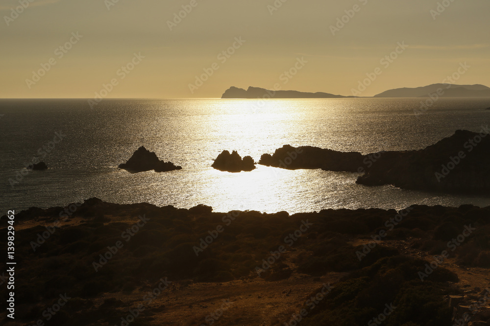 Paesaggio in controluce all'ora del tramonto con l'acqua che si illumina di un color oro acceso e la costa e le isolette sono in silhouette
