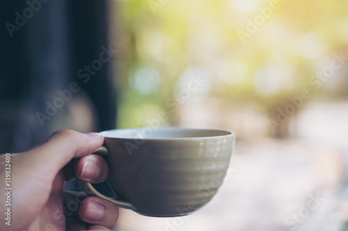 Hand holding clay tea mug with green nature background