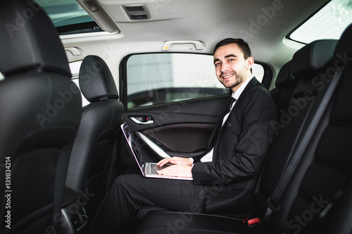 Handsome young businessman working on his laptop while sitting in the car and look at camera © F8  \ Suport Ukraine