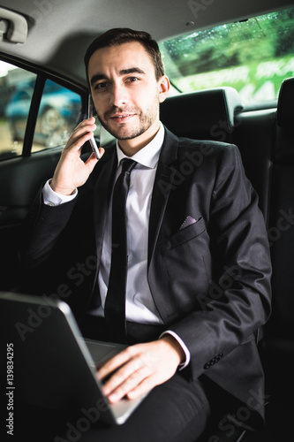Handsome young businessman working on his laptop and talking on the phone while sitting in the car © F8  \ Suport Ukraine