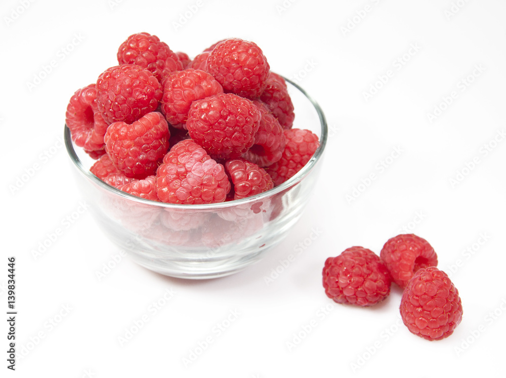Red raspberries in a glass bowl with three loose berries on a white background Red raspberries in a glass bowl with three loose berries on a white background