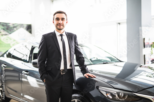 relaxed young businessman or salesman with hands crossed in front of car