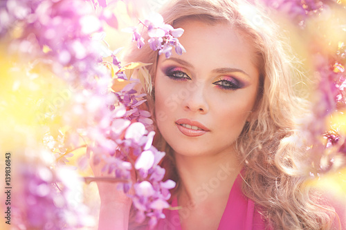 Fashion portrait of young beautiful girl posing against lilac bushes in blossom