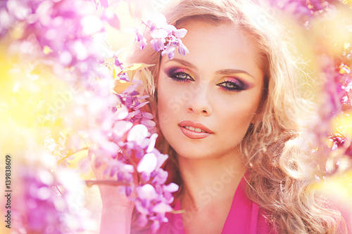 Fashion portrait of young beautiful girl posing against lilac bushes in blossom