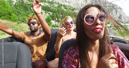 Cheerful multi ethnic students enjoying vacation driving in red convertible 