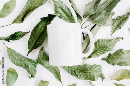 Blank template of white mug and green leaves on white background. Flat lay, top view.