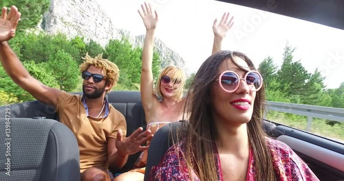 Cheerful multi ethnic students enjoying vacation driving in red convertible 