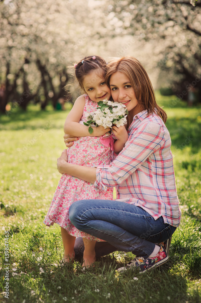 spring vertical portrait of happy mother and kid daughter on the walk in blooming cherry garden. spring vertical portrait of happy mother and kid daughter on the walk in blooming cherry garden.
