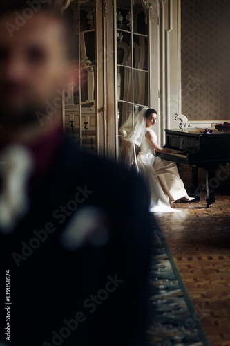 elegant gorgeous bride playing the fortepiano and stylish handsome groom posing in rich old room. sensual look. unusual luxury wedding in retro style. photo