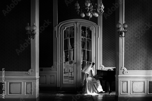 elegant gorgeous bride playing the fortepiano in rich old room. sensual look. unusual luxury wedding in retro style. black and white photo photo