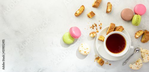 Cup of black tea with tasty almond cookies, rich in vitamins, minerals and varicolored macaroons  on a white background in light key. Top view , copy space.