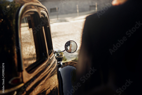 Φωτογραφία unusual view on luxury elegant wedding couple hugging, reflection in mirror of hands at stylish black car