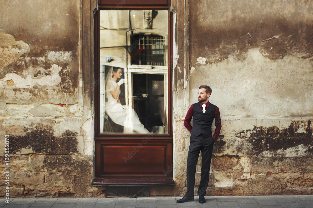 elegant gorgeous bride drinking coffee in window and stylish groom posing at building in street outdoors cafe. unusual luxury wedding couple in retro style. romantic moment. elegant gorgeous bride drinking coffee in window and stylish groom posing at building in street outdoors cafe. unusual luxury wedding couple in retro style. romantic moment.