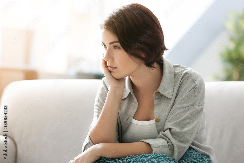 Depressed young woman sitting on sofa at home Depressed young woman sitting on sofa at home