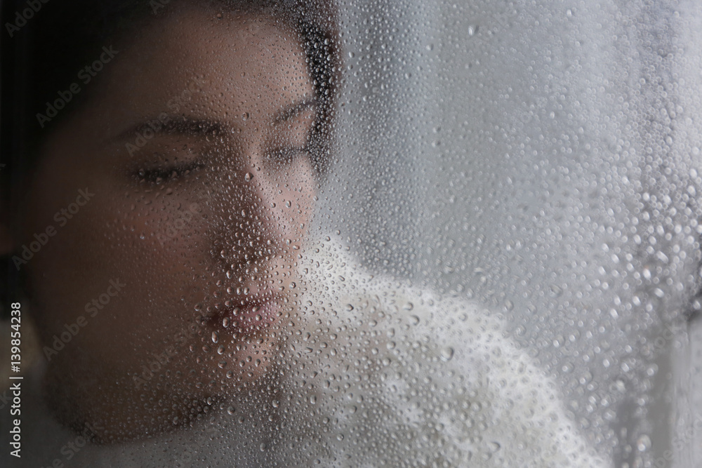 Portrait of depressed young woman near steamy window, view from outside