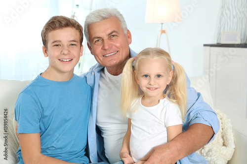 Cute children with grandfather sitting on sofa in living room
